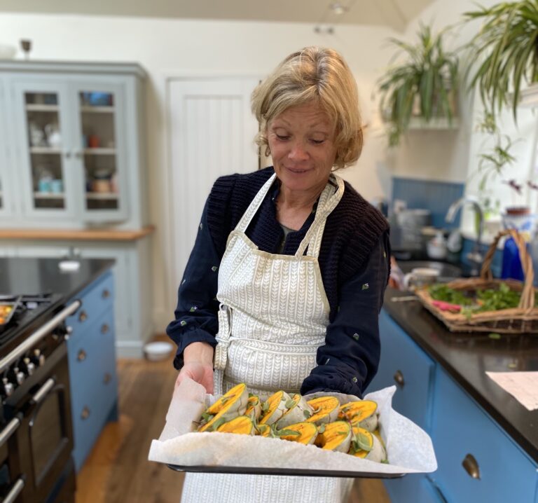 A lady with a white apron holding a tray full of roasted pumpkins, in a blue kitchen