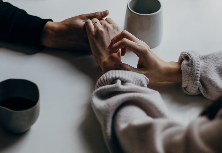 A close up image of a man and woman holding hands on a coffee table with two cups next to them